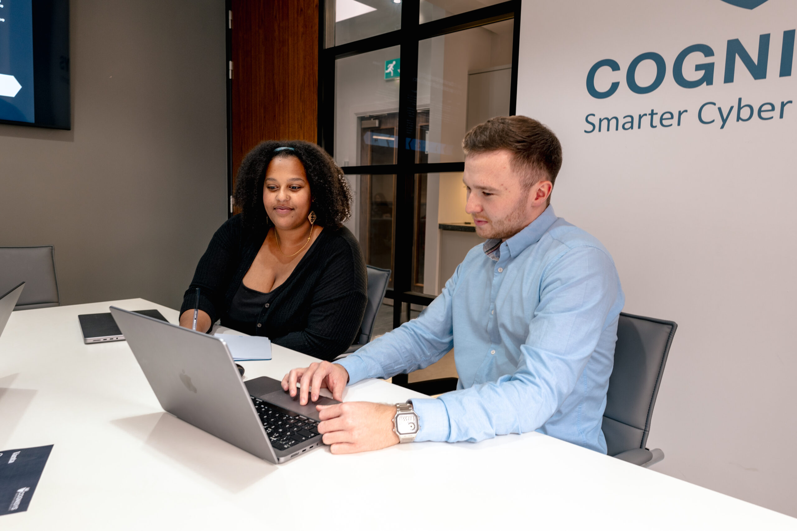 Two cyber security consultants reviewing information on a computer screen, discussing recent cyber attacks and vulnerabilities.