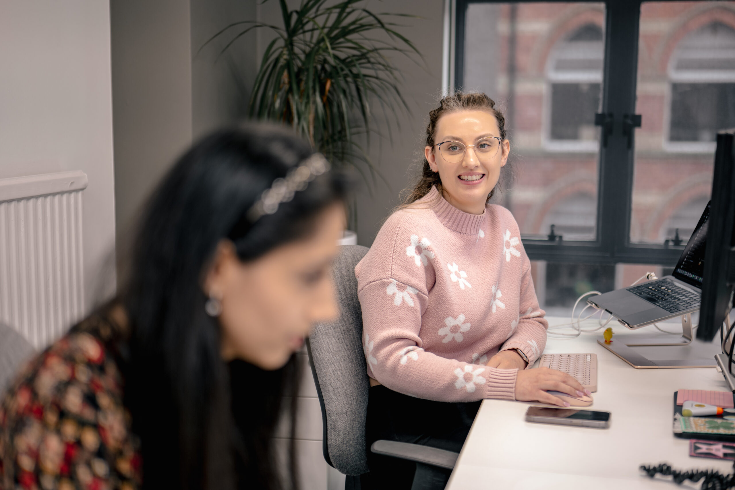 Two cyber security consultants engaged in a discussion while working on their computers, emphasising collaboration in tackling social engineering challenges