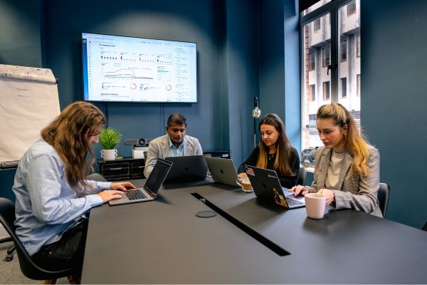 Cybersecurity professionals in a meeting room reviewing a vulnerability management platform displayed on a screen as part of a strategic discussion on security scans and vulnerability remediation.